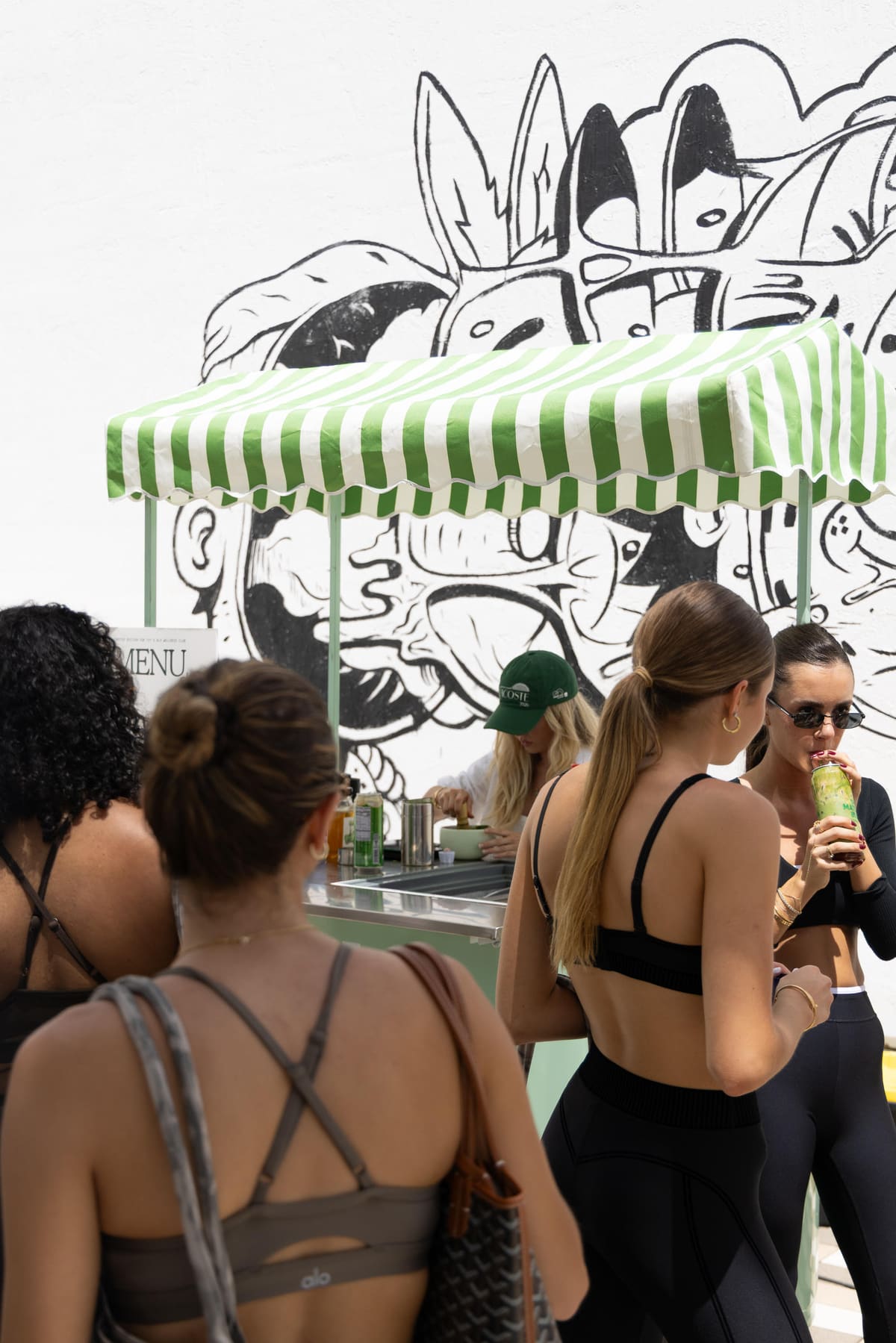 Crowd ordering matcha at the striped-awning cart in front of a black and white mural