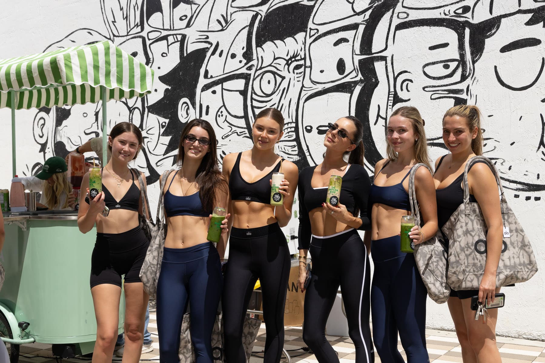 Crowd holding Matcha Bike cans in front of the mural